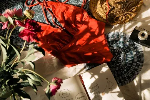 Flatlay of red bikini with straw hat, open sketchbook and flowers – summer fashion inspiration